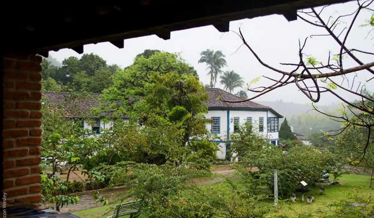 Fachada do casarão histórico da Fazenda Santa Rita em Muqui, cercado por natureza e jardins.