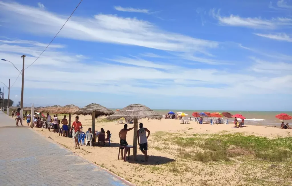 Quiosques de sapê na orla da Praia das Neves, em Presidente Kennedy, com mar calmo ao fundo