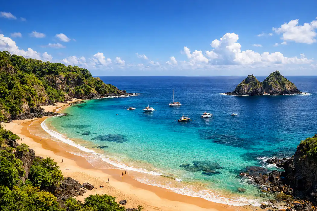 Vista panorâmica da Baía do Sancho em Fernando de Noronha, com mar azul-turquesa e falésias verdes.