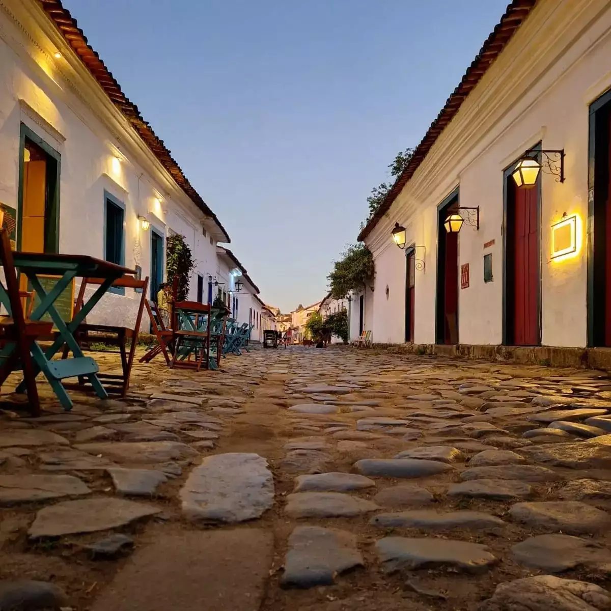 Rua de pedras irregulares no Centro Histórico de Paraty com a Igreja de Santa Rita e barcos coloridos ao fundo.