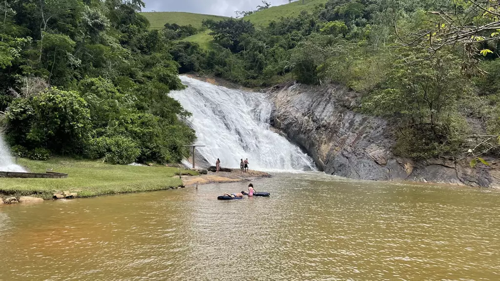 Vista panorâmica da Cachoeira Rio do Meio em Santa Leopoldina, mostrando a ampla queda d'água rochosa e a área de banho com banhistas aproveitando a piscina natural