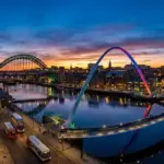 Vista panorâmica das pontes iluminadas sobre o Rio Tyne em Newcastle, Inglaterra, ao anoitecer.