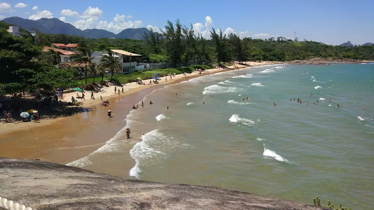 Vista da Praia dos Adventistas em Guarapari com castanheiras fazendo sombra natural na areia e mar calmo.