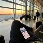Viajante usando aplicativo de celular para buscar passagens aéreas baratas em um aeroporto.
