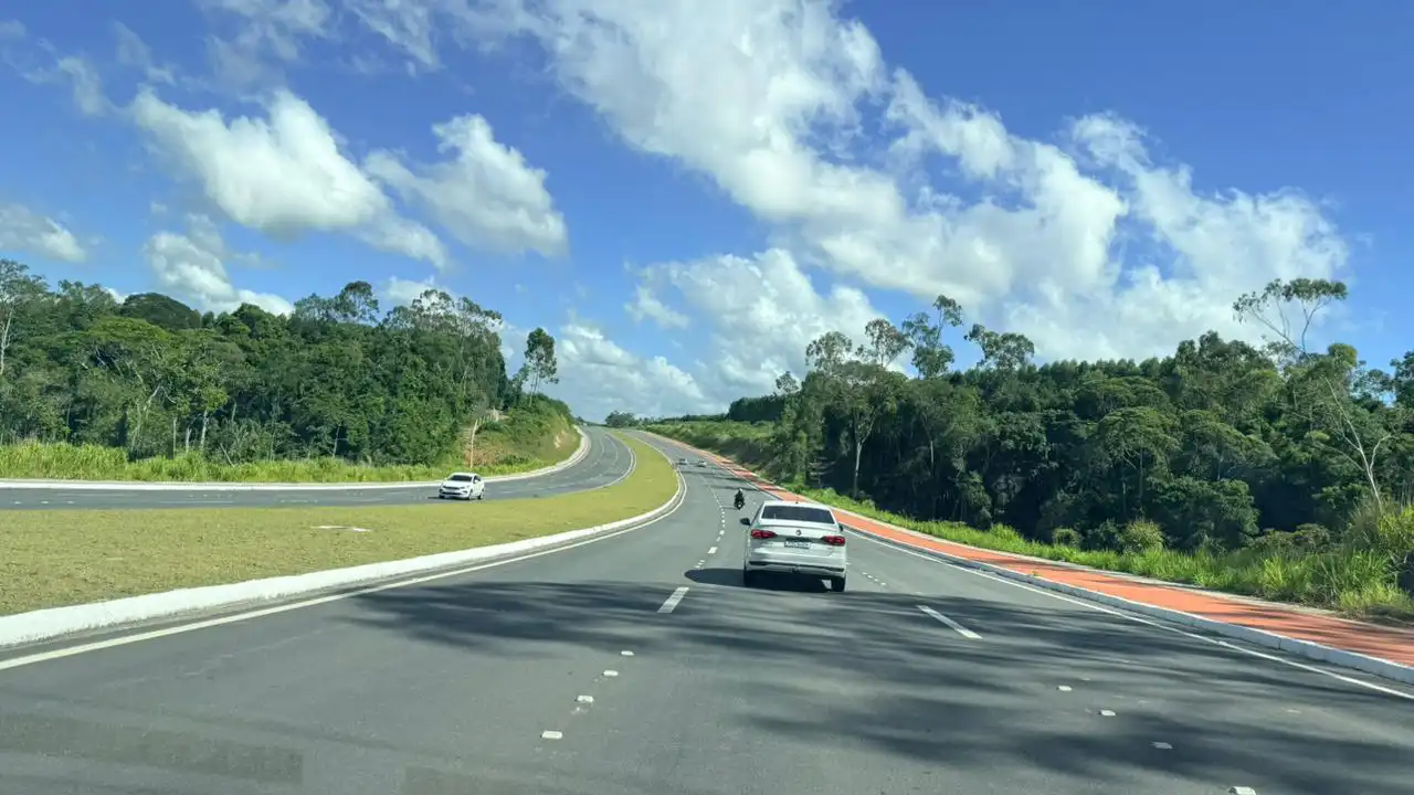 Vista da nova Rodovia ES-115, o Contorno de Jacaraípe, na Serra, Espírito Santo. A imagem mostra pistas duplas asfaltadas, sinalização moderna e fluxo livre de veículos em dia de sol.