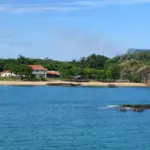 Vista panorâmica da Praia da Casa do Governador em Vila Velha, cercada por mata e pedras, vista a partir do Parque Cultural.