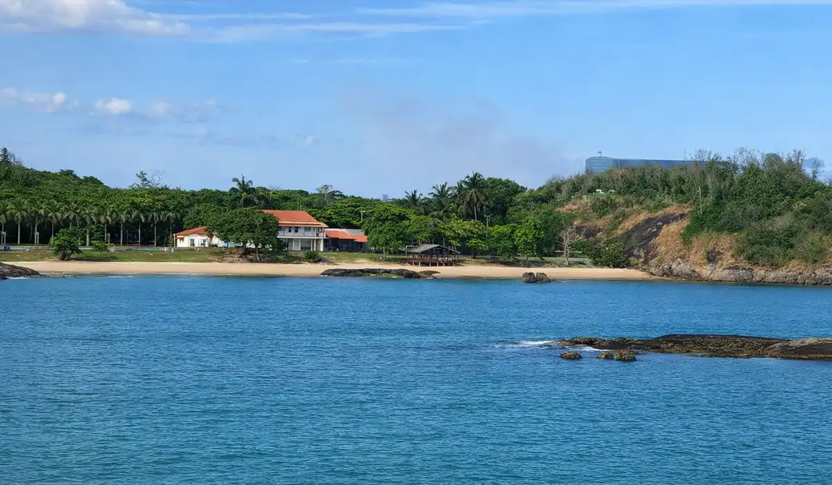 Vista panorâmica da Praia da Casa do Governador em Vila Velha, cercada por mata e pedras, vista a partir do Parque Cultural.