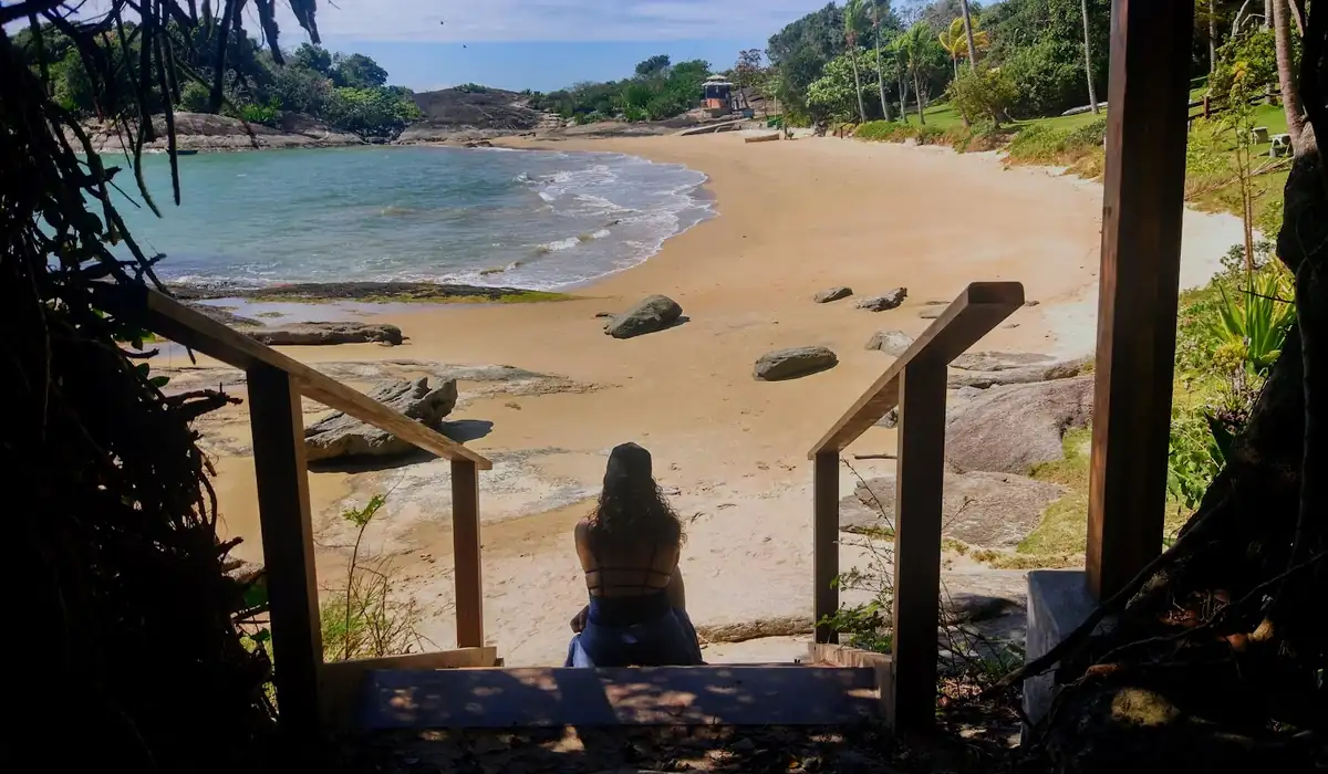 Vista da Praia dos Ventos em Guarapari, com mar calmo e transparente e pedras na lateral.